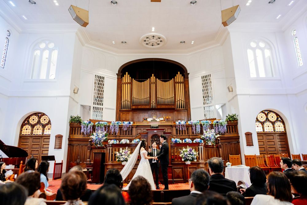 Wedding ceremony setting inside a traditional church with white walls, arched windows, and wooden pews.