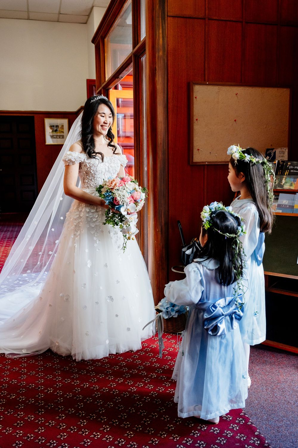 Two people in formal attire share a tender moment on red carpeted hallway with wooden walls.