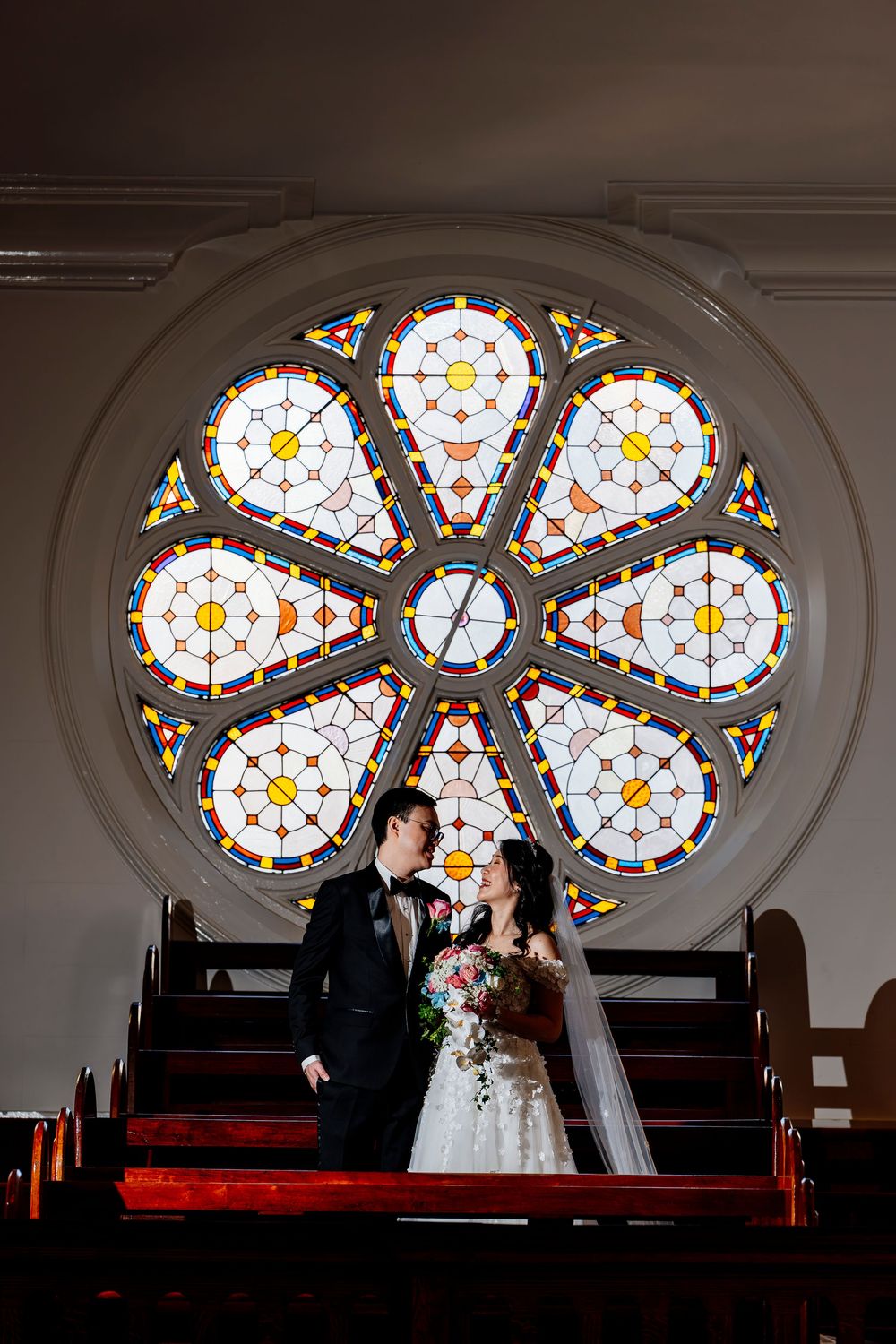 A series of silhouetted figures are framed by a beautiful stained glass rose window in a church setting.