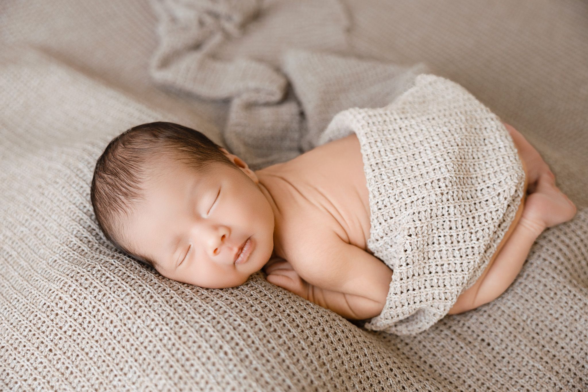A sleeping newborn photography session featuring delicate white lace swaddles and soft neutral tones.