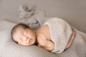 Sleeping baby wrapped in knitted beige blanket lays peacefully on soft textured surface.