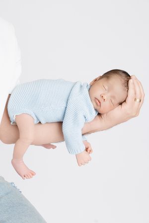 A sleeping baby wearing light blue stripes lies on a soft white blanket.