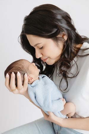 A tender moment between mother and baby in a light-filled studio series of photos showing gentle affection and care.