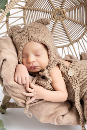 Sleeping baby with tan knit hat captured in artistic newborn photography with striped overhead lighting.