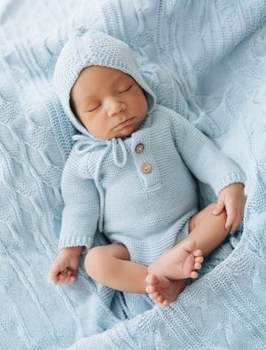 Peaceful newborn baby sleeping in a blue knit romper and bonnet hat on a soft blue blanket.