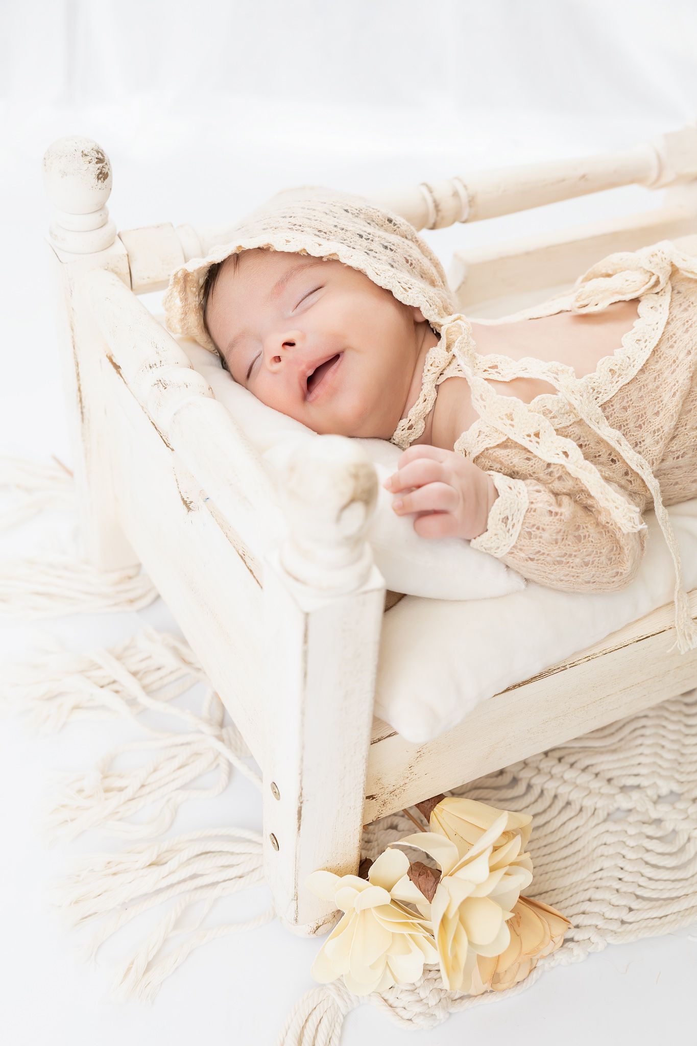 Sleeping baby swaddled in delicate vintage lace with pale yellow flower details against white bedding.