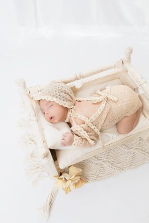 Newborn nestled in soft cream lace fabric and bedding with yellow floral accents in dreamy natural lighting.