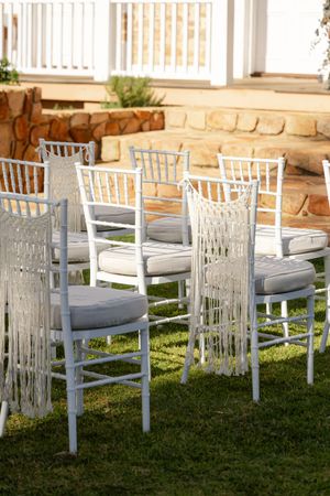 White Chiavari chairs with macrame backdrops and gray cushions arranged on green grass for an outdoor wedding.