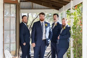 Groomsmen in navy blue suits share a candid moment together outside on a sunny day.
