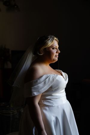 Profile silhouette of bride in elegant off-shoulder wedding dress against dark background.