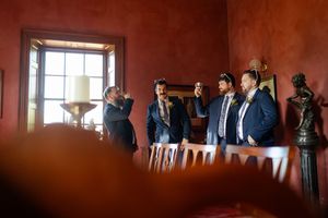 Wedding party gathered in a rustic red-walled room with natural light streaming through windows.