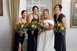 Group of bridesmaids in navy dresses stand together with bouquets celebrating with bride.