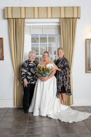 bride family photo share a joyful moment in an elegant room with beige curtains, one wearing a flowing white wedding gown.