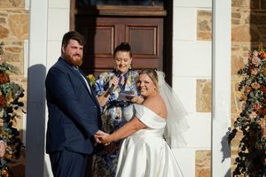 A wedding couple stand with their celebrant outside a stone entrance with decorative florals.