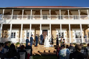 Wedding guests gathered on a grand white wraparound porch of a historic mansion during an outdoor celebration.