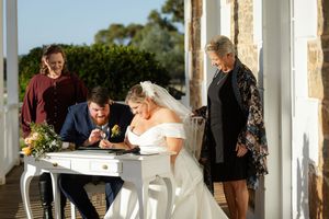Wedding ceremony taking place on a stone porch with document signing at a white table.