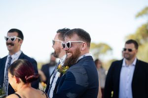 Groomsmen and wedding guests sharing laughs and conversation outdoors during a sunny celebration.