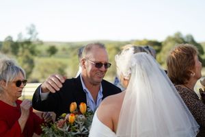 Wedding party celebrates outdoors on a sunny day with rolling hills in the background.
