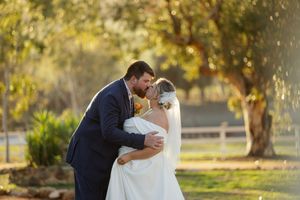 A couple shares romantic kisses in an outdoor setting with golden autumn trees and sunlight in the background.