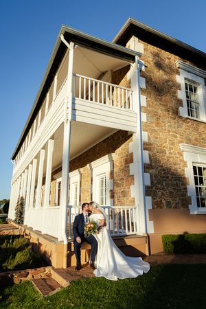 White colonial style wedding venue with stone accents and wraparound porch at sunset. Buckland Estate wedding venue