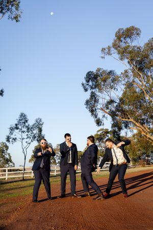 Wedding party poses playfully in a line on red earth with trees in the background.