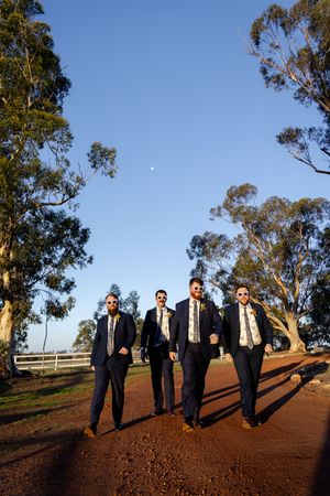 Formal group walks along dirt path with eucalyptus trees against bright blue sky.