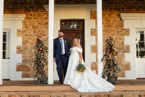 Wedding couple poses on rustic stone porch with floral decorations and wooden door.