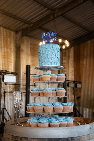 A tiered display of light blue cupcakes and small wedding cake arranged on a rustic wooden stand with champagne glasses.