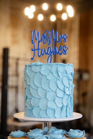 Light blue textured wedding cake with script topper displayed under warm lighting.