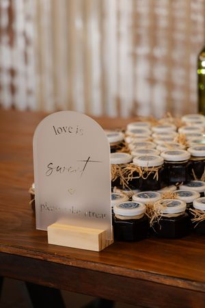 Small white place cards with handwritten text displayed in wooden holders next to mason jar favors on rustic table.