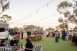 Outdoor wedding reception setup with string lights and rustic wooden tables during golden hour.
