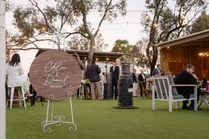 Outdoor wedding ceremony setup with wooden arch signs and string lights at dusk.