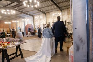 bride and groom walking in a modern industrial wedding venue with string lights and guests in the background.