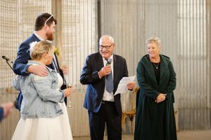 A group gathers during a wedding speeches in an industrial space with corrugated metal walls.