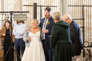 Wedding ceremony guests gathered in an industrial-style venue with metal railings and white curtains.