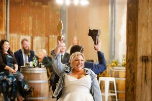 Candid wedding reception moment with guests laughing and dancing in a rustic wooden beam venue with warm lighting.