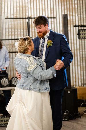 Couple sharing a dance while bride wears a denim jacket over her wedding dress.
