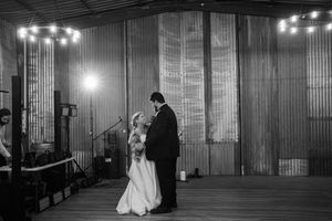 Black and white photo of a couple dancing in an industrial venue with string lights overhead.