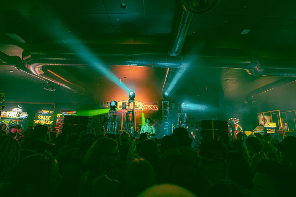 A glowing green nightclub interior with laser lights and silhouettes of people dancing on a crowded dance floor.