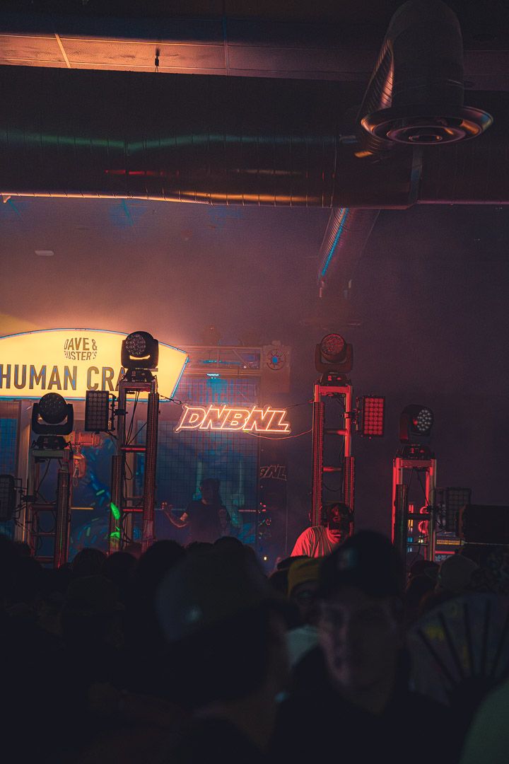 Dark nightclub interior with neon lighting and equipment silhouettes against illuminated stage setup.