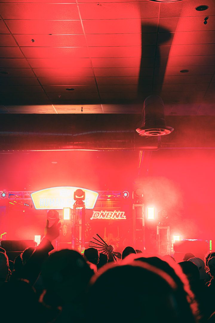 Concert crowd silhouetted against bright red stage lighting and illuminated venue ceiling.