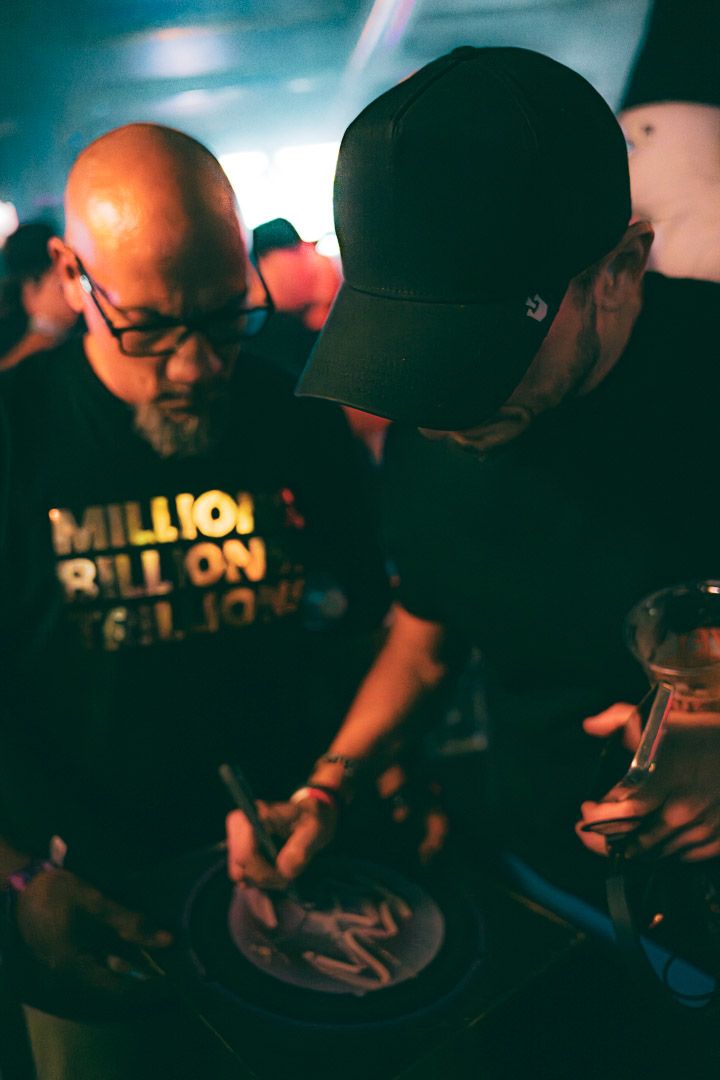 Concert attendees signing merchandise at dimly lit venue.