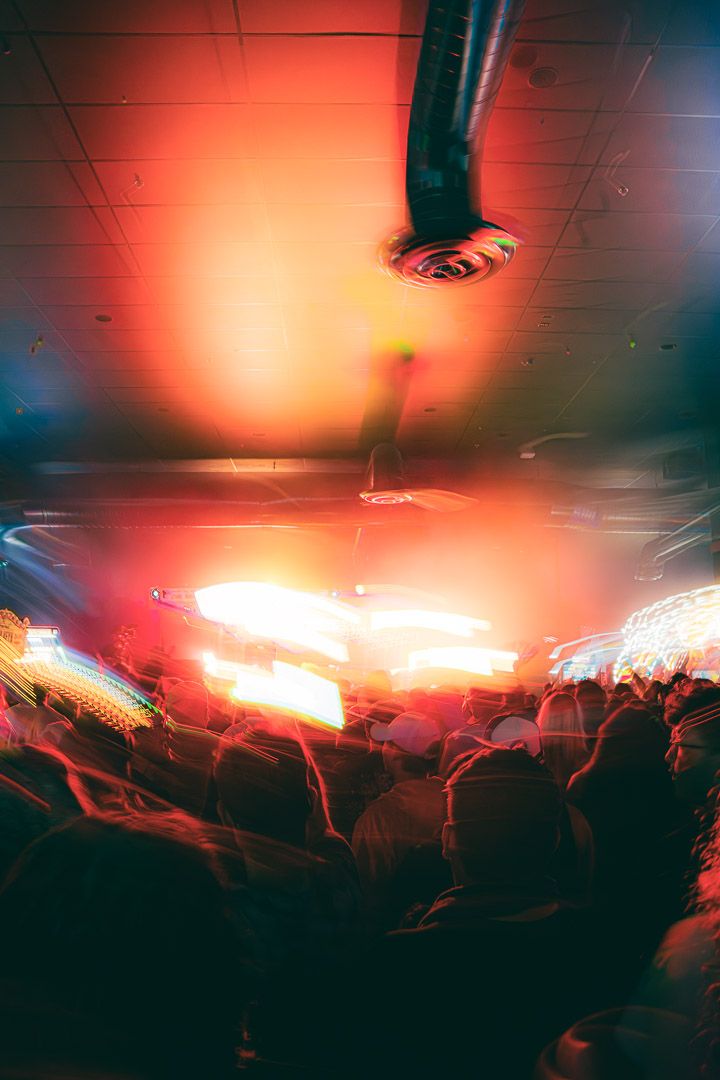 Concert crowd silhouettes beneath red stage lights and ceiling spotlights creating an atmospheric nightlife scene.
