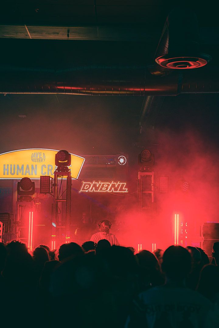 Music festival stage bathed in red light with 'HUMAN' text visible and silhouetted audience in foreground.