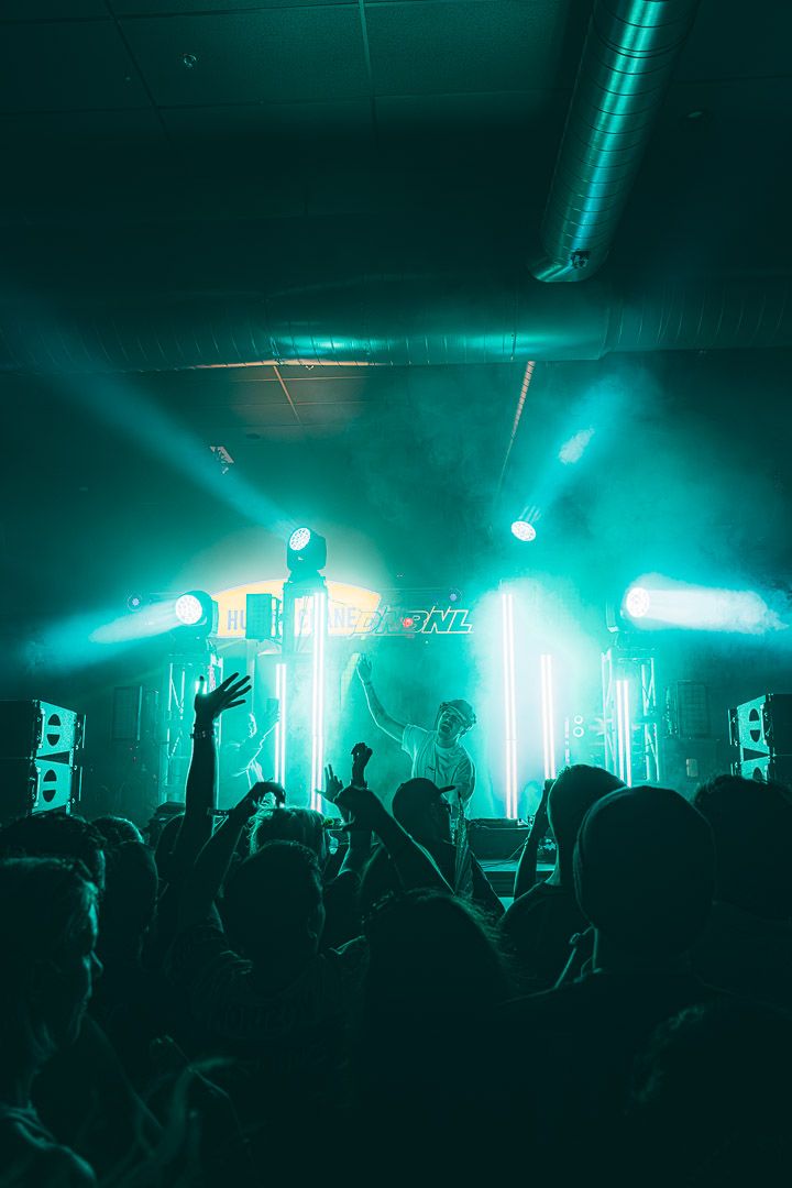 Concert crowd in silhouette against turquoise stage lighting at an electronic music show.