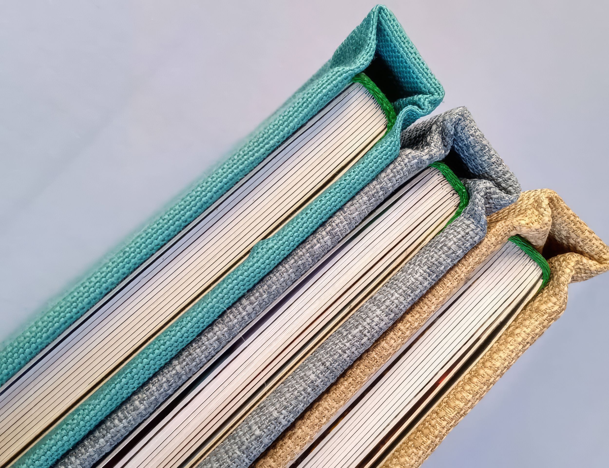 Stack of premium photo album spines in teal, white, and gold fabric textures on gray background.  Fotógrafo en Formosa