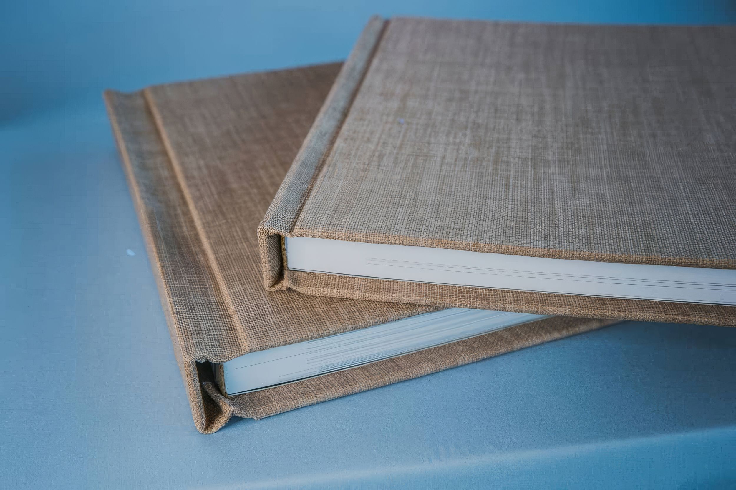 Two linen-covered hardcover photo albums stacked on a light blue surface.  Fotógrafo en Formosa