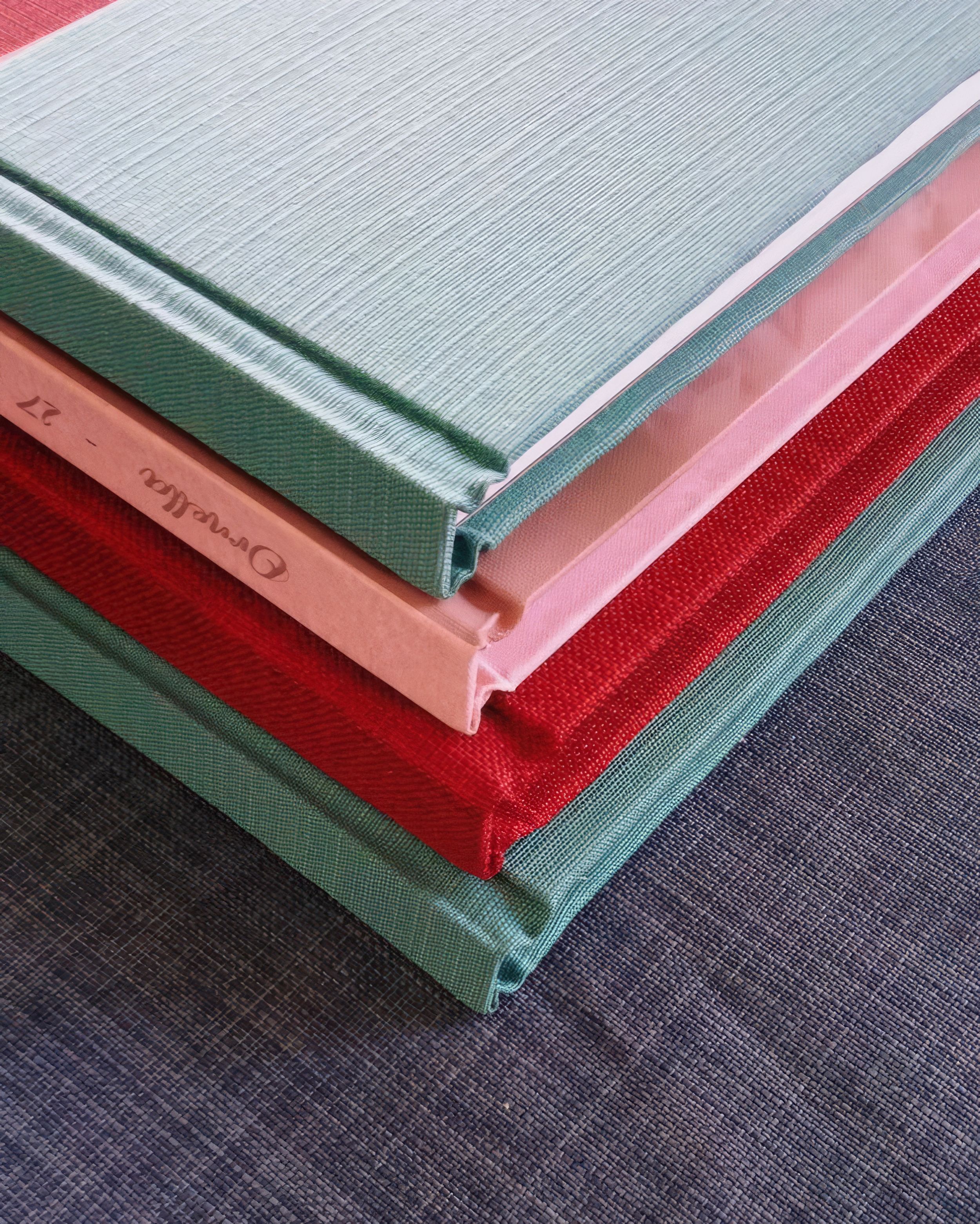 Stack of colorful fabric hardcover photo albums in teal, pink, and red.  Fotógrafo en Formosa