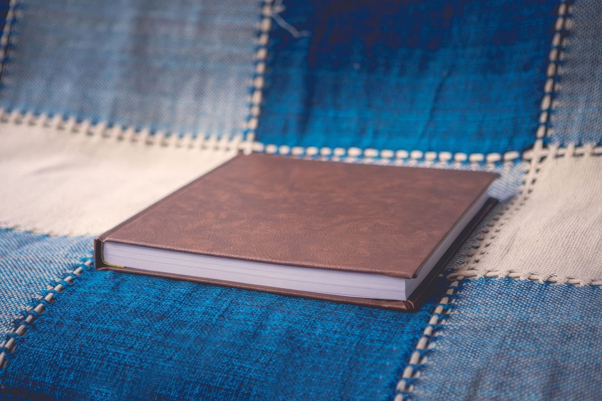 Brown leather hardcover photo book resting on a patchwork denim quilt background.  Fotógrafo en Formosa