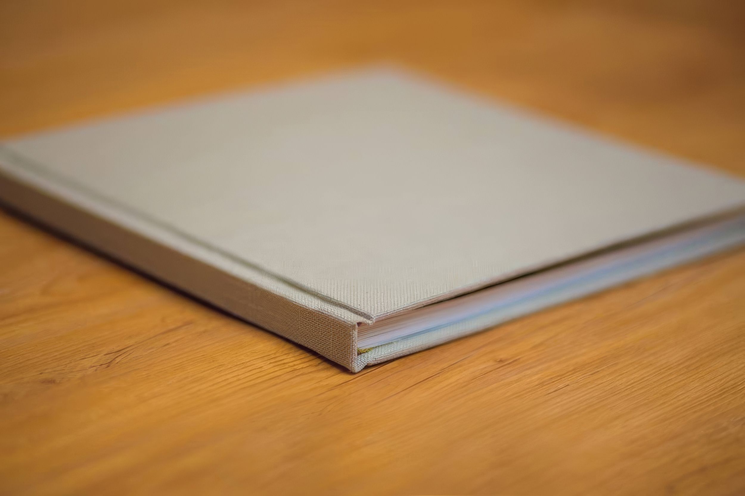 Side view of a gray linen hardcover photo book on a wooden table.  Fotógrafo en Formosa